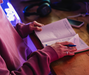 Vue resserée sur un bureau et des main féminines posées sur un carnet, stylo à la main