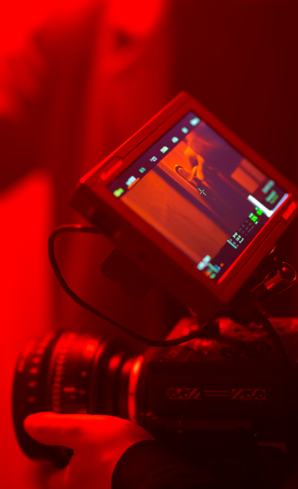 Gros plan sur l'écran d'une caméra de tournage en train de filmer dans une ambiance rouge.